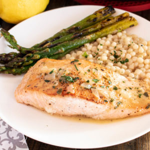 pan seared salmon with white wine lemon sauce on white plate with couscous and asparagus