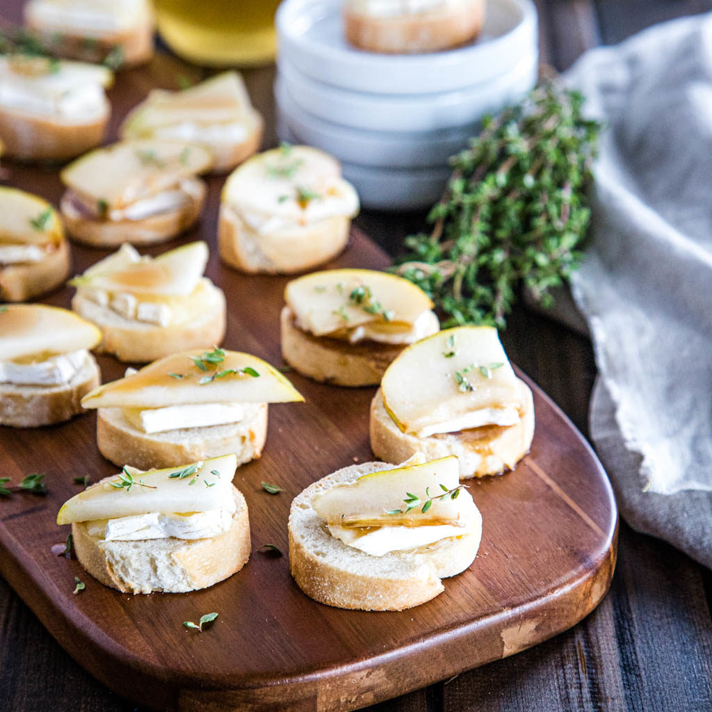 Serving board of brie and pear crostini with honey-balsamic glaze and fresh thyme
