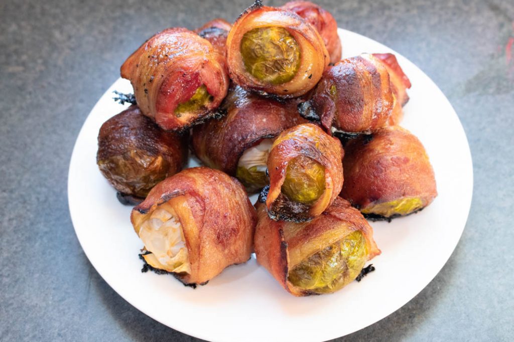 bacon wrapped brussels sprouts stacked on round white plate