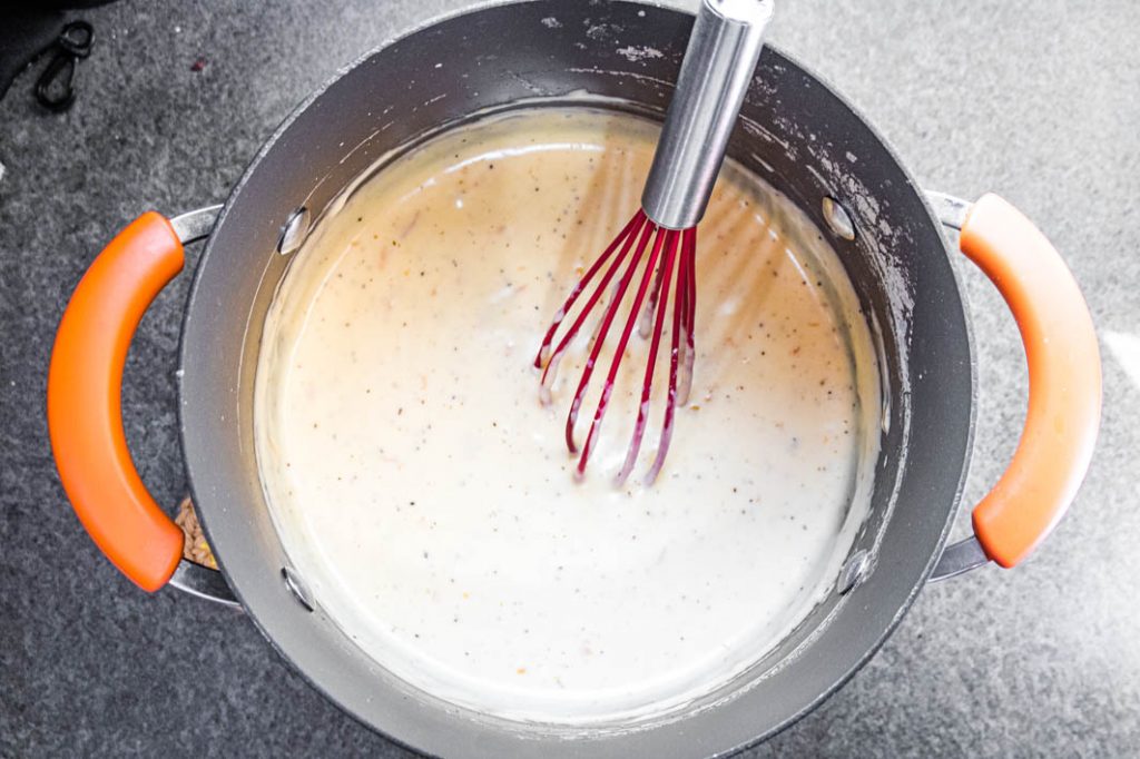 cheese sauce in pot with red whisk