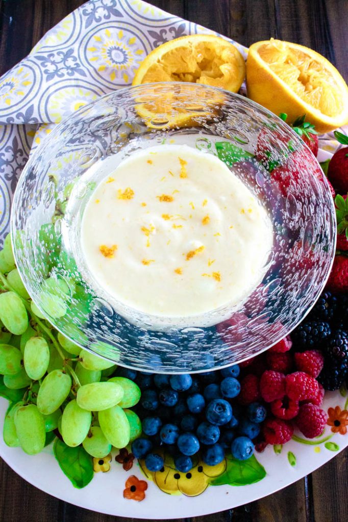 orange creamsicle fruit dip in glass bowl with variety of fruits on a platter