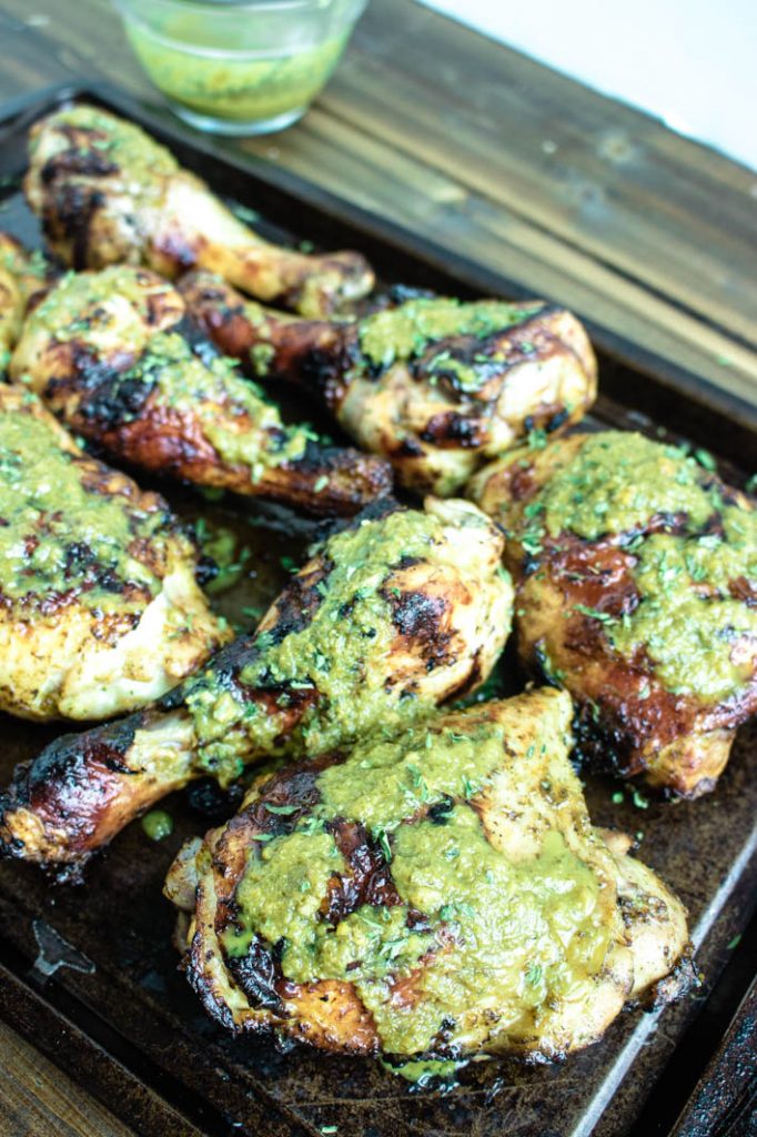 citrus-marinated chicken pieces with green sauce on baking pan